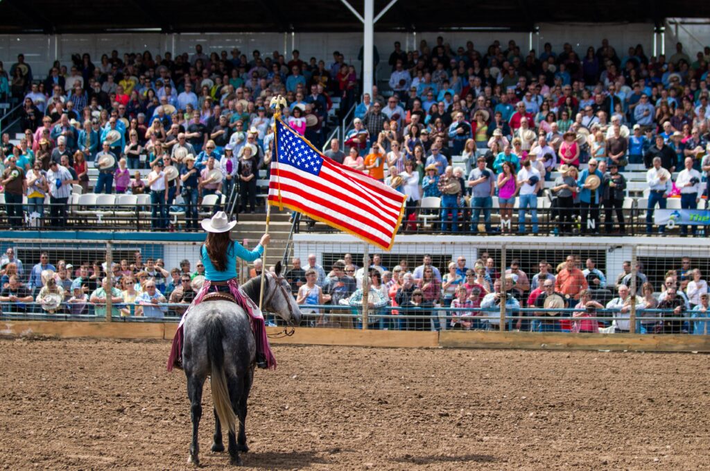 A horse and rider, carrying an American Flag in front of a crowd at a rodeo.